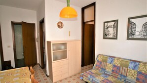 Ein gemütlicher Raum mit einem Holzkasten, einem gemusterten Sofa und einem Esstisch mit Stühlen.