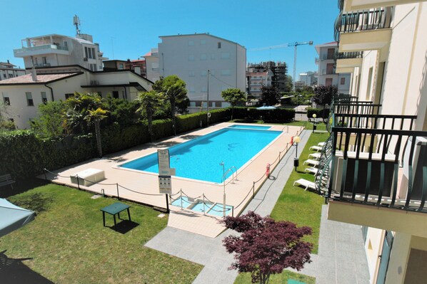 Une piscine rectangulaire dotée d’un plongeoir, entourée d’une clôture basse et d’une pelouse avec un banc.