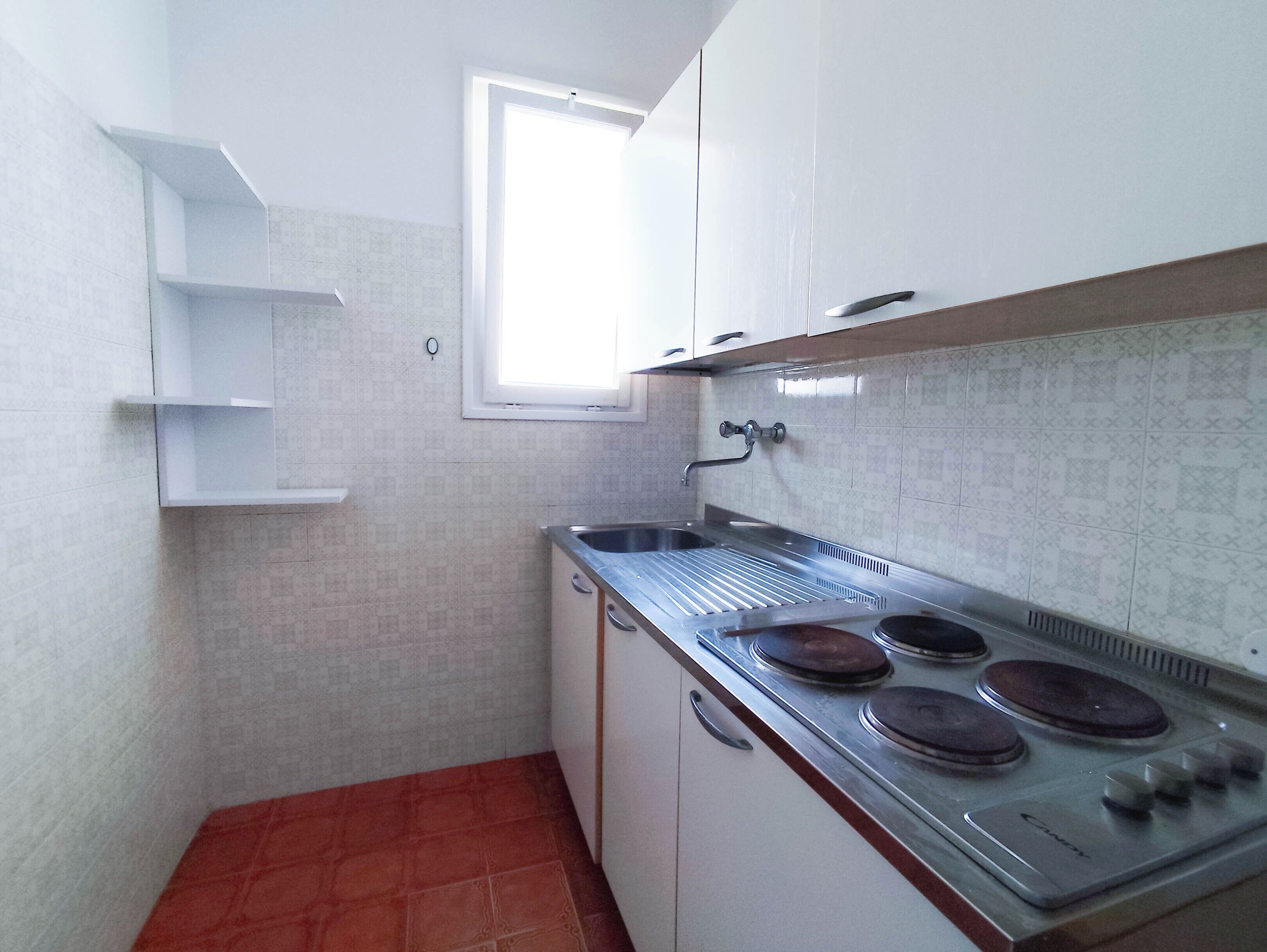 A compact kitchen with white cabinets, a stainless steel sink, and a gas stove.