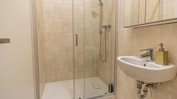 Un baño moderno con ducha envuelta en vidrio, un lavamanos blanco y un espejo sobre él.