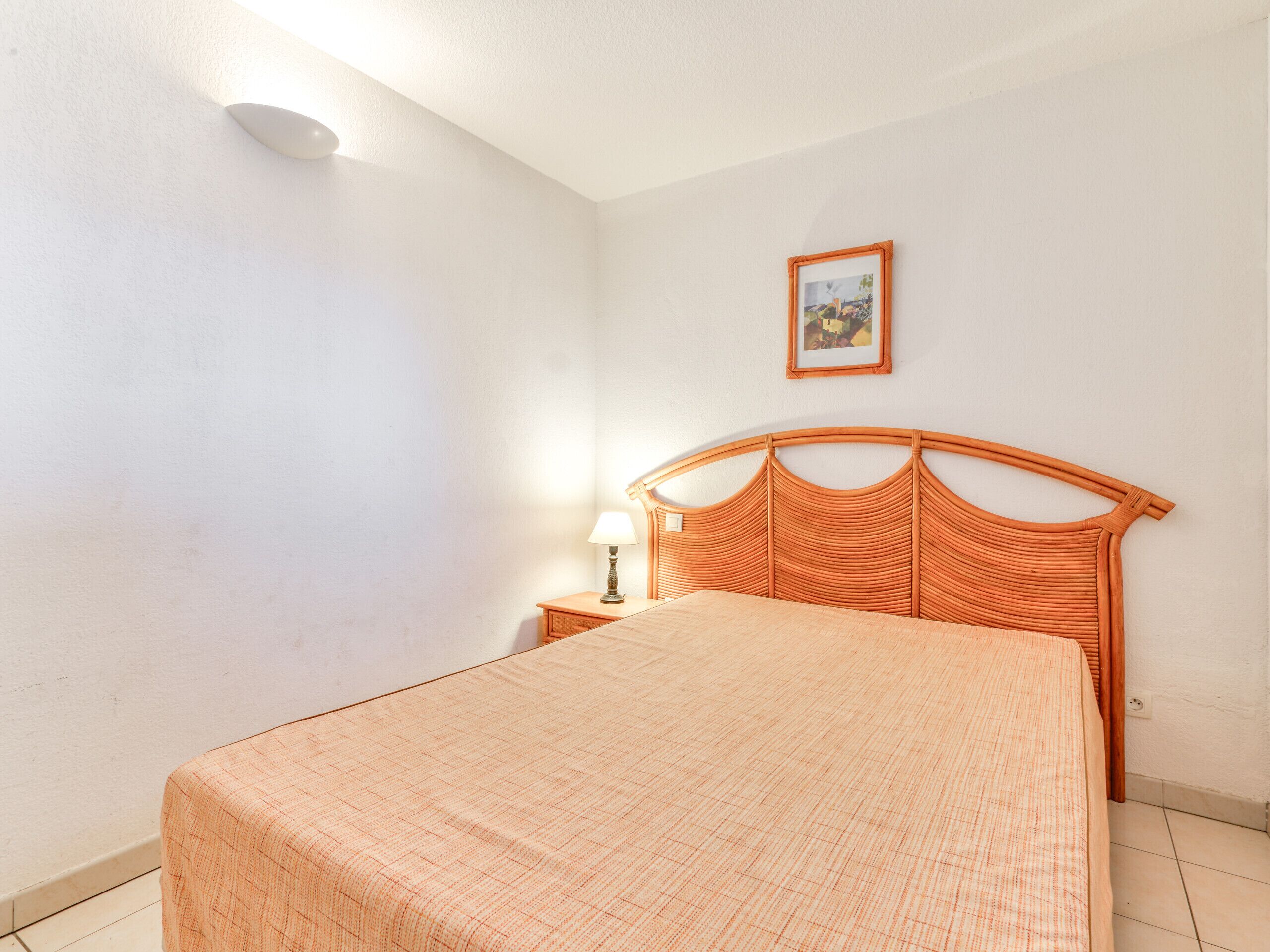 A bedroom with a single bed, a nightstand, a wall-mounted picture, and a ceiling light.