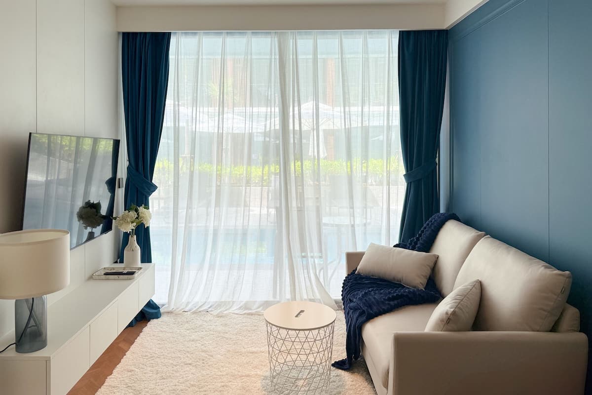 Ein modernes Wohnzimmer mit einer Couch, einem runden Couchtisch, einer Lampe und einem großen Fenster mit Vorhängen.