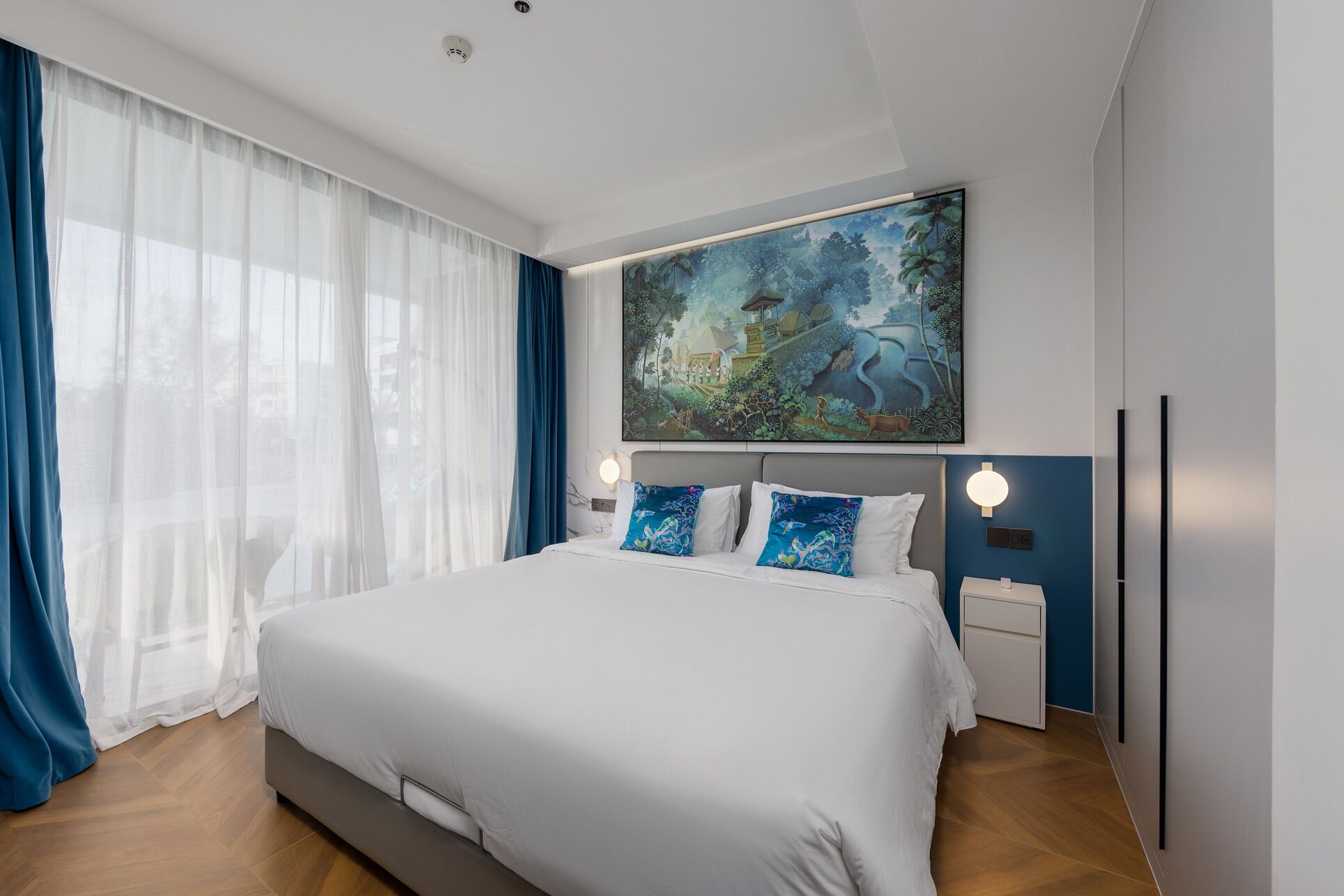 Una camera d'hotel moderna con un letto grande, un quadro sopra il letto e vista all'esterno attraverso tende trasparenti.