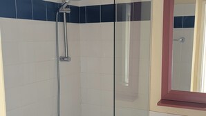 Ett badrum med en duschkabin med glasväggar, en vit tvättställ och en spegel med en röd ram.