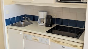 Ett kompakt kök med diskmaskin, kaffebryggare, mikrovågsugn och diskho.