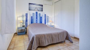 Ein Schlafzimmer mit einem Bett, zwei Nachttischen mit Lampen, einer Wand-Klimaanlage und einem Gemälde eines Piers.