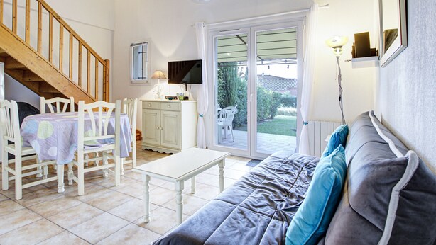 Ein gemütliches Wohnzimmer mit Sofa, Sesseln, einem Tisch, einem Fernseher und einer Treppe.