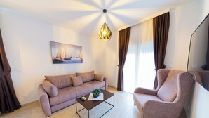 A living room with a sofa, armchair, coffee table, and a painting of sailboats. - Spacious 1BR Apt for 3 w/ Terrace & Pool (Sutomore)