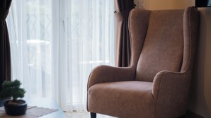 A brown armchair in a room with a large window and a potted plant on a small table. - Spacious 1BR Apt for 3 w/ Terrace & Pool (Sutomore)