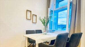 Un coin repas avec une table blanche, quatre chaises noires, un vase avec une plante et une fenêtre avec des rideaux.