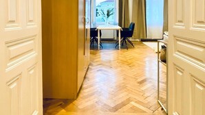 Un couloir doté d’un parquet en bois disposé en chevrons, un coin repas avec une table et des chaises, et une vue sur un bâtiment à l’extérieur, visible par une fenêtre.