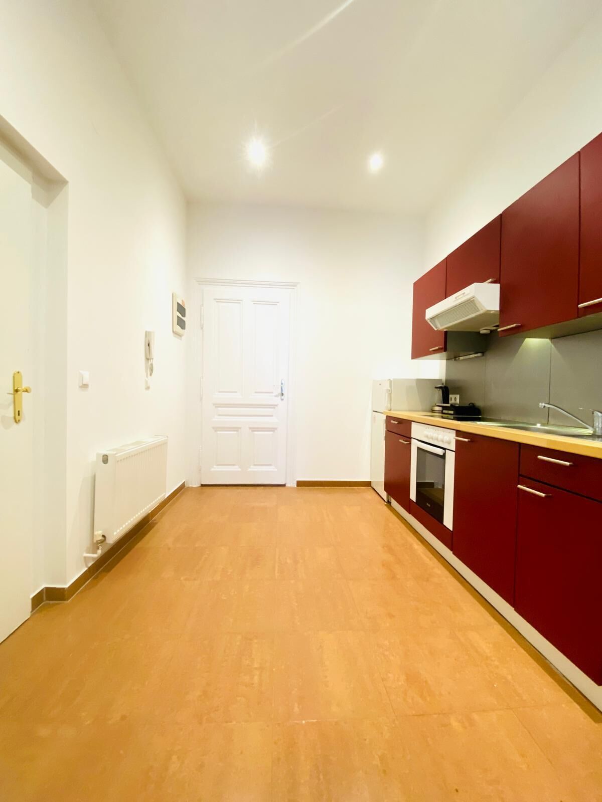 Una cocina con armarios rojos, una puerta blanca y un radiador.