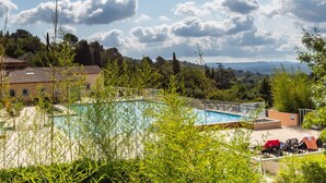 Piscina cercada por vegetação, com vista para montanhas e um edifício ao fundo.