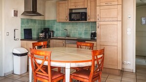Una cucina con un tavolo rotondo, quattro sedie di legno, un forno a microonde e un cestino per i rifiuti.