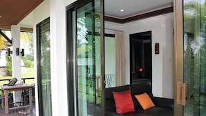 Een moderne woonkamer met een glazen deur die uitkomt op een balkon, een zwarte leren bank met rode en oranje kussens, en een kleine tafel met stoelen.