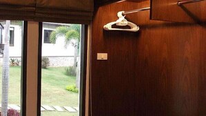 Een kamer met houten kasten, een raam met uitzicht op een tuin, en een witte kleerhanger aan de muur.