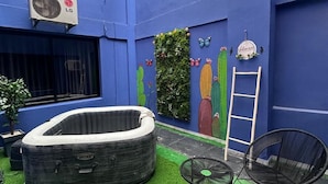 Une cour aux murs bleus, avec un jacuzzi gonflable, deux fauteuils en osier, une petite table et une échelle appuyée contre le mur.