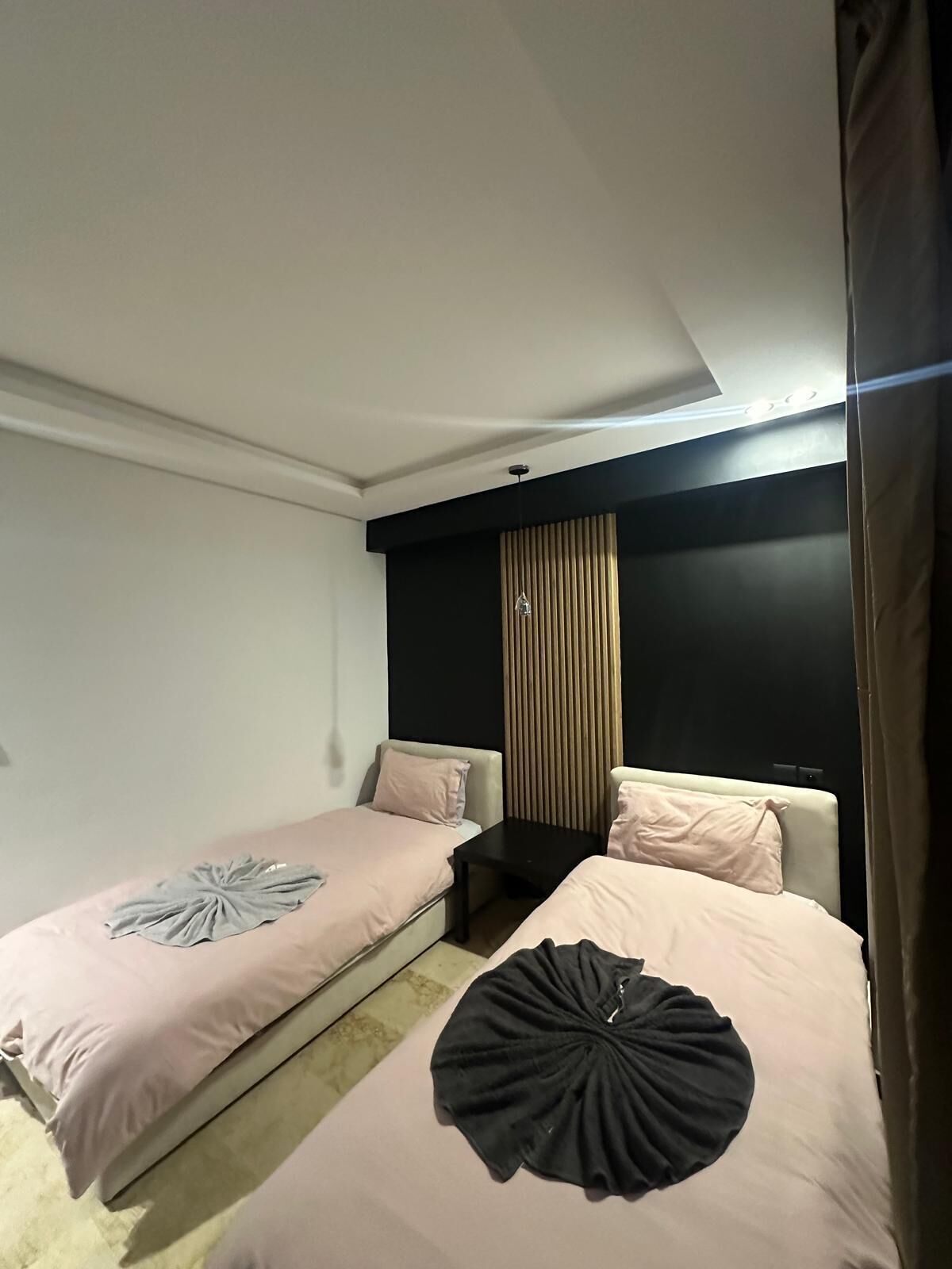 Een hotelkamer met twee bedden, een zwart hoofdbord, een tafeltje en een gordijn.