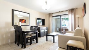 Un salon moderne comprenant un coin repas, un canapé, un téléviseur et un balcon agrémenté de rideaux.
