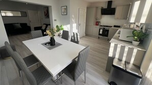 Ett modernt kök med en matplats, med ett vitt bord, grå stolar och en liten krukväxt.