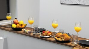 A breakfast setup with croissants, pastries, fresh fruits, and orange juice on a wooden table. - Designer Apt 2BDR/8P – 2 Baths, Batignolles (Paris)
