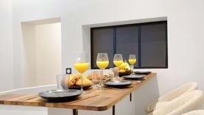 Mesa de café da manhã posta com croissants, copos de suco de laranja e uma tigela de frutas.