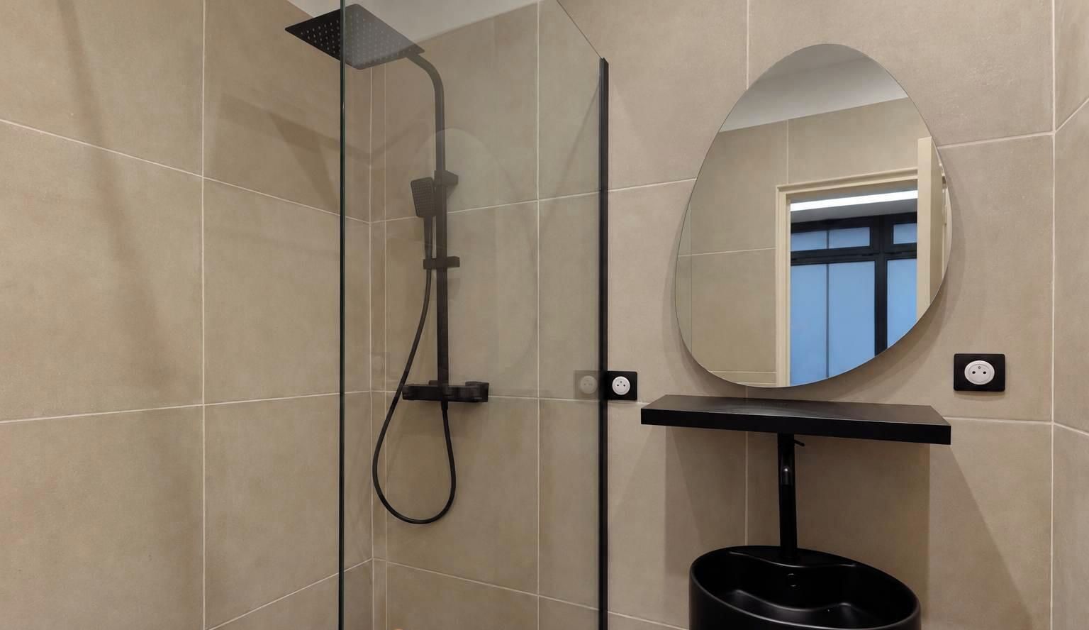 Un baño moderno con ducha de vidrio, espejo redondo y lavamanos negro.