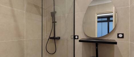 Un baño moderno con ducha de vidrio, espejo redondo y lavamanos negro.