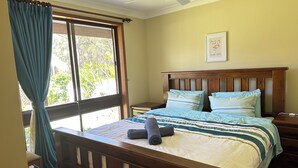 Une chambre à coucher avec un lit en bois, un ventilateur de plafond et une fenêtre avec des rideaux.