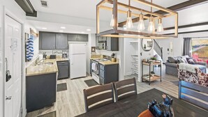 A modern kitchen with a central island, a dining area with a wooden table, and a living room with a sofa and a decorative bowl. - Ski In Ski Out Condo at Bear Mountain! HOT TUB! Walk Onto Chair Lift 9! (Big Bear Lake)