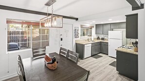 A modern kitchen with dark cabinets, a central island, and a dining area with a wooden table and chairs. - Ski In Ski Out Condo at Bear Mountain! HOT TUB! Walk Onto Chair Lift 9! (Big Bear Lake)