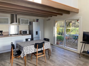 Une cuisine moderne équipée d’une cuisinière à gaz, d’un four à micro-ondes et d’un réfrigérateur. On y trouve une table à manger avec des chaises, ainsi qu’une grande porte-fenêtre coulissante donnant sur un jardin.