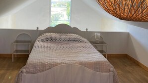 Ein Schlafzimmer mit einem Bett, zwei Nachttischen, einer Hängelampe und einem Fenster mit Ausblick.