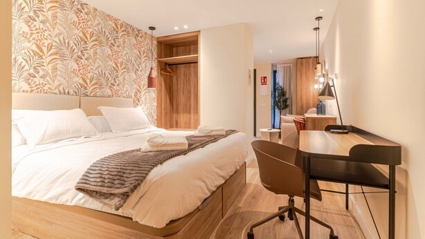 Habitació d'hotel moderna amb un llit gran, un panell de capçalera de fusta, un escriptori amb una cadira i un mirall.