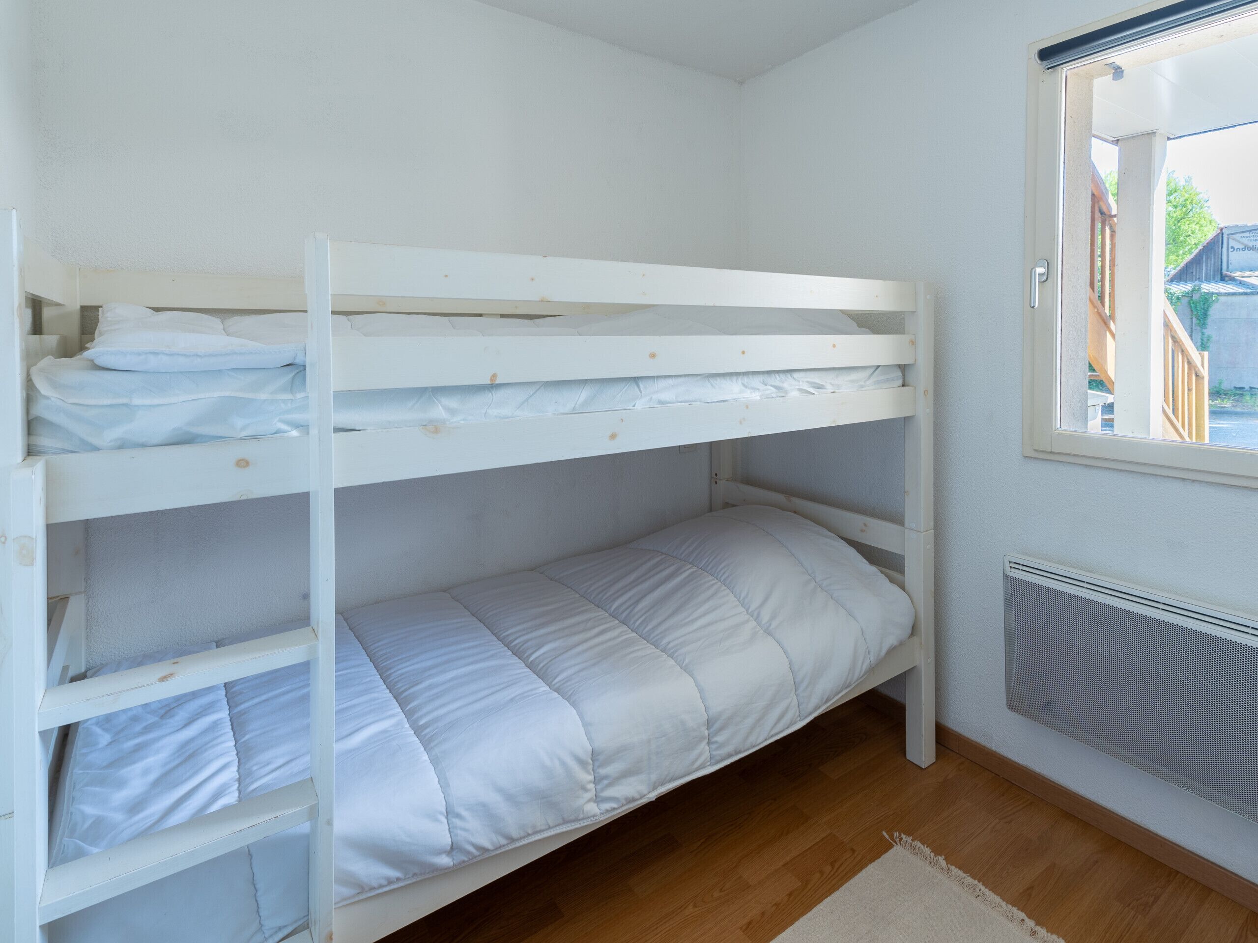 Une chambre avec un lit superposé, du linge de lit blanc, une fenêtre avec vue et un radiateur.