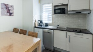 Een kleine keuken met een vaatwasser, een magnetron, een koffiezetapparaat en een raam met zonwering.