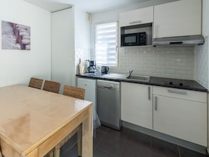 A compact kitchen with a dishwasher, a microwave, a coffee maker, and a window with blinds.