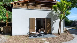 Een gebouw met twee verdiepingen, een balkon, een overdekte patio met twee rieten stoelen en een kleine tuin.