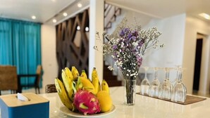 Zona de recepción de un hotel con un frutero que contiene plátanos y una pitaya, un jarrón con flores y una caja de pañuelos.
