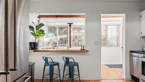 Una cocina moderna con encimera de madera, dos taburetes azules, una planta en maceta y vistas al exterior por la ventana.