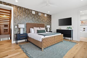 A modern bedroom with a wooden bed, a TV mounted on the wall, and a patterned wallpaper. - Book for ACL | Lake Austin Views | Pool, Firepit + Game Room | Sundown Social (Austin)