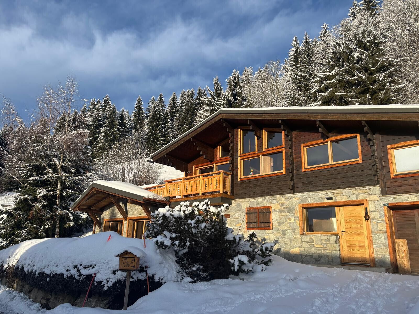 A multi-story wooden cabin with a stone foundation, surrounded by snow-covered trees and a clear sky.