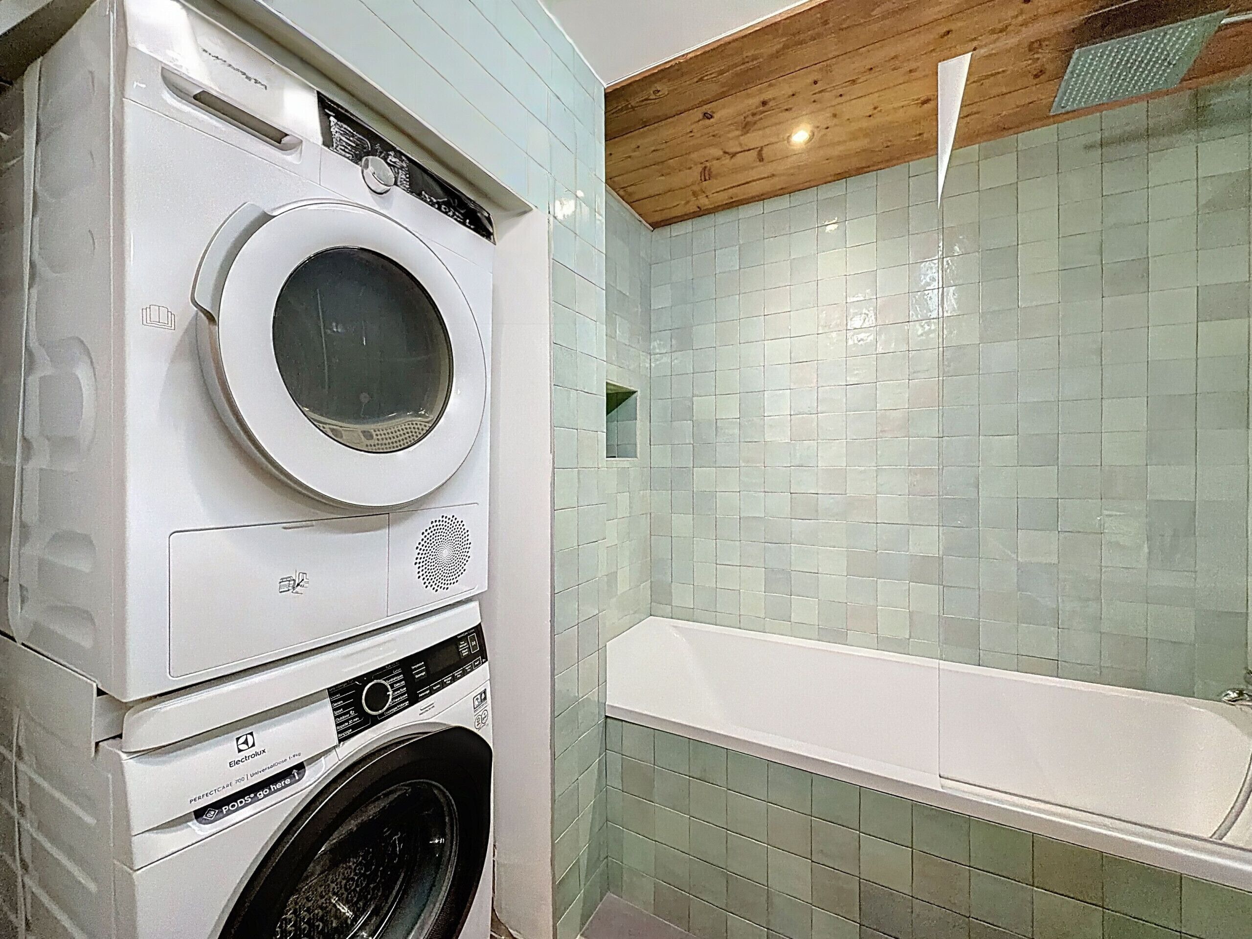 A compact bathroom with a washing machine, a bathtub, and tiled walls.