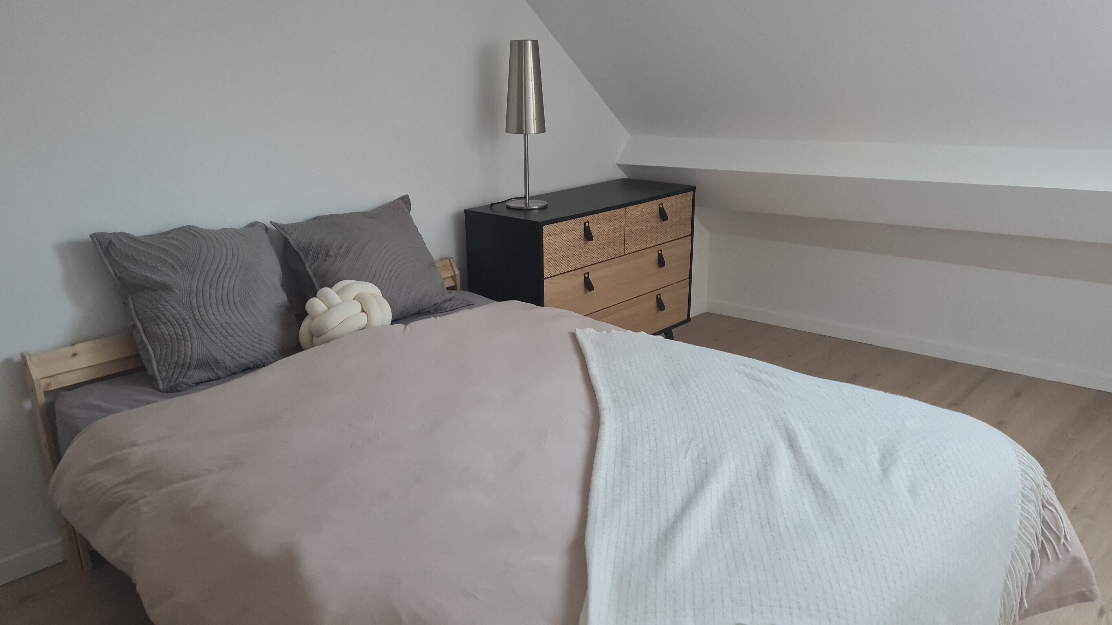 A bedroom with a bed, pillows, a bedside table, and a lamp.