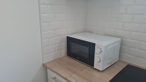 Un microondas blanco sobre una encimera de madera en una cocina con paredes de azulejos blancos.