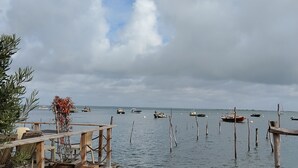 Une jetée en bois qui mène à une plage de sable, avec des bateaux sur l’eau et un ciel nuageux.