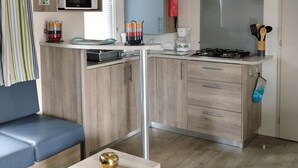 Une cuisine compacte équipée d’un four à micro-ondes, d’une cuisinière et de placards. On y trouve un canapé bleu et une petite table agrémentée d’un objet décoratif.
