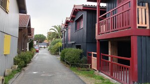 Une rue étroite bordée de maisons traditionnelles en bois dotées de balcons, un ciel dégagé et une voiture garée.