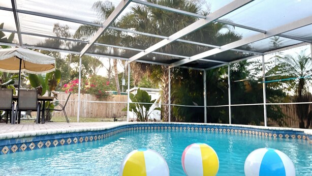 Una piscina con tres pelotas de playa, un porche cubierto y una cerca de madera al fondo.