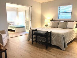 Ein Schlafzimmer mit Bett, Stuhl, Nachttisch, Lampe und einem Fenster mit Jalousien.
